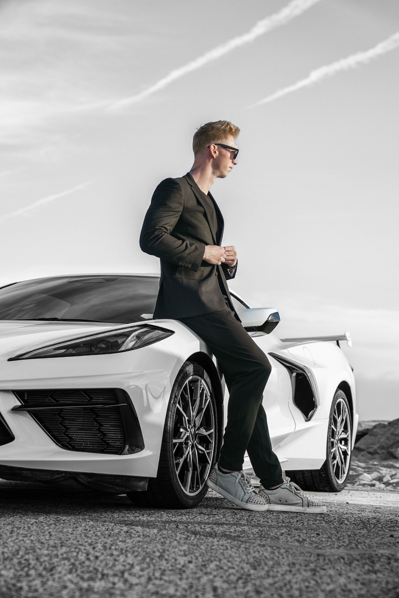 Parker in a black suit beside a white Corvette